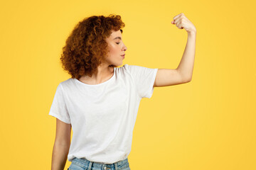 Confident strength curly young lady student in white t-shirt show muscles biceps on hand