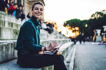 Fototapeta premium Portrait of cheerful hipster girl with electronic stylus and portable pc resting at city historic center