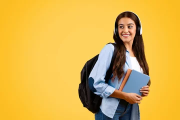 Fotobehang Smiling calm young student lady typing in headphones, with backpack, enjoy music, lifestyle © Prostock-studio