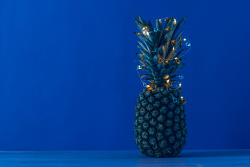 Christmas pineapple with lighted garland on dark blue background with copy space.