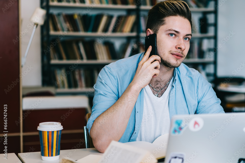 Poster serious man speaking on smartphone at table while studying in library