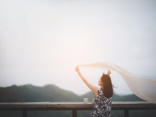 A woman with long hair wearing a dress with her arms spread up and a shawl flowing in the wind. The concept of leisure travel - obrazy, fototapety, plakaty