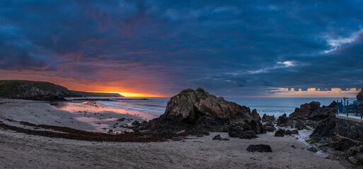 Beautiful sunrise landscape image of Kennack Sands in Cornwall UK wuth dramatic moody clouds and vibrant sunburst