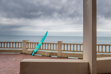une terrasse avec un surf posé sur la rambarde devant l'océan et un ciel nuageux