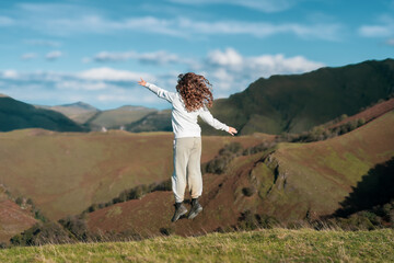 une jeune enfant saute en l'air  au bord d'un précipice devant un paysage de montagnes - 666754817