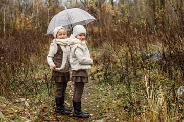 Fototapeta premium Portrait of young twin girls standing under an umbrella in the park, looking at the camera.