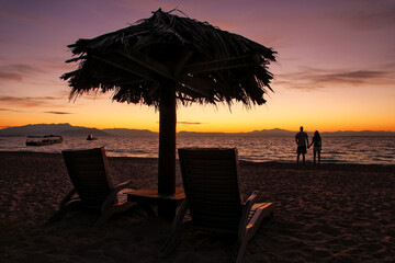 Silhouetted sun chairs with thatched umbrella on a beach at sunrise