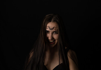 Evil laughing at the top of her voice, the witch looks into the camera on a black background in the twilight. On Halloween, a female witch grinning in a terrible grin looks at the camera.