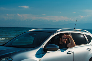 Handsome young man in sunglasses driving car on seashore at summer day