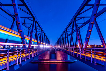 Fototapeta na wymiar Two symmetrical steel railway bridges at night with train light trail on the left. Stars on the sky. Long exposure photo. 