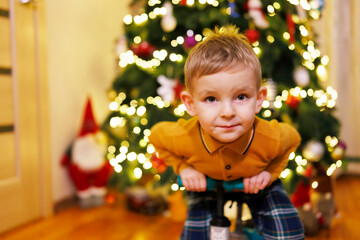Happy little child boy sitting on push bicycle on a Christmas tree background