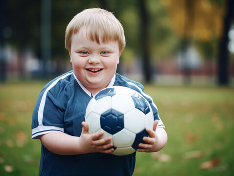 Smiling boy with syndrome down holds ball in a summer park.