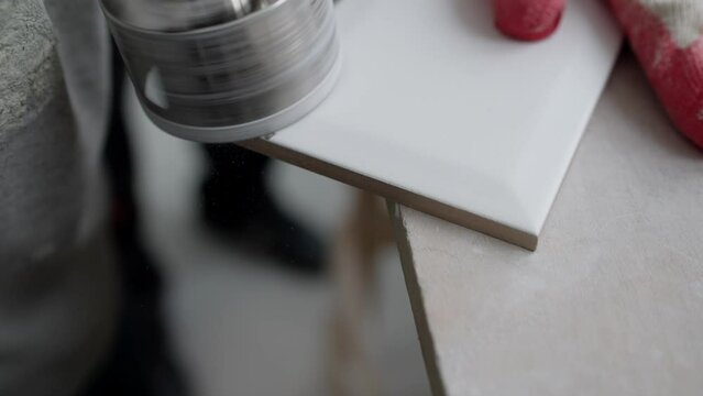 A tiler cuts a hole in a ceramic tile. A worker uses a unique special tool to drill a hole in a ceramic tile. The process of drilling holes in ceramic tiles.