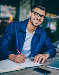 Portrait of skilled caucasian male student writing in notepad enjoying learning using laptop...