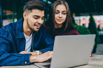 ,smiling teen hipsters using netbook for searching information via wifi connection at cafe terrace