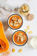 Roasted butternut squash soup with cream and pumpkin seeds on two white mugs.