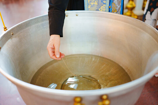 The priest's hand dips a chain with a cross into the water of the baptismal font