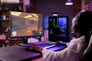 Woman in brick wall living room playing science fiction video game on gaming PC at computer desk,...