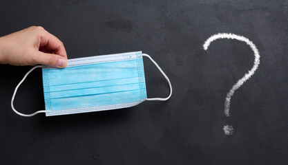 A woman's hand holds a disposable medical mask on a black chalk board background