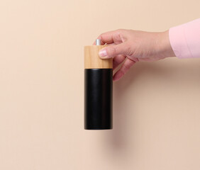 Female hand holding a wooden pepper mill on a beige background