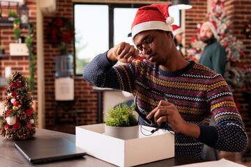 Sad man in santa hat gathering personal office things from desk after getting fired on christmas eve. Upset startup company employee discharged from job during winter seasonal holiday