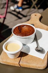 Savor a delicious chocolate brownie with vanilla sauce, served on a wooden holder with a silver spoon, in a cozy outdoor hipster cafe Vertical image