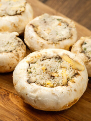 Stuffed mushrooms cups on a wooden board and table. High quality product with breadcrumbs, cheese and herbs ready for oven cooking.