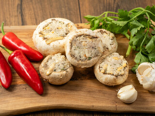 Stuffed mushrooms cups and chilly peppers and garlic cloves on a wooden board and table. High quality product with breadcrumbs, cheese and herbs ready for oven cooking.