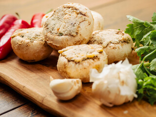 Stuffed mushrooms cups and chilly peppers and garlic cloves on a wooden board and table. High quality product with breadcrumbs, cheese and herbs ready for oven cooking.