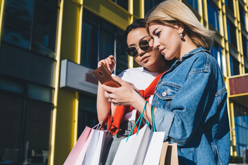 Young blonde watching phone with friend in street