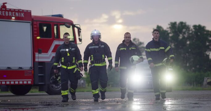 Brave Firefighters Team Walking to the Camera. In Background Paramedics and Firemen Rescue Team Fight Fire in Car Accident, Insurance and Save Peoples Lives concept.