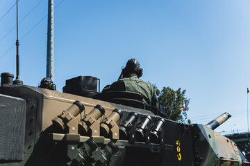 Rear view of focused soldier with headphones standing inside the tank. Blue sky and beautiful sunshine during military parade. High quality photo