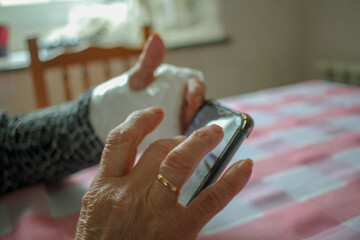 elderly woman with a cast wrist watching a mobile phone