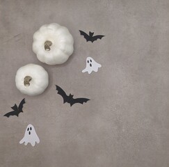 Two white pumkins, bats and ghosts on gray cement background.