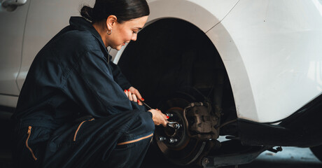 Hardworking female mechanic changing car wheel in auto repair workshop. Automotive service worker...