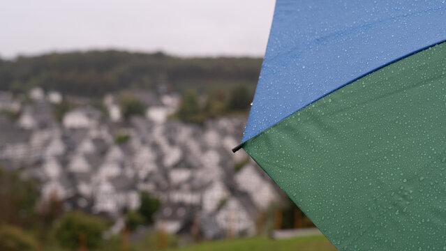 Woman stands in the rain with an umbrella and enjoys the view of an old town with half-timbered houses. Selective focus
