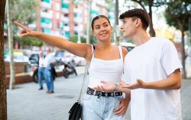 Romantic happy young couple walking on city streets on summer day, pointing while looking at something interesting