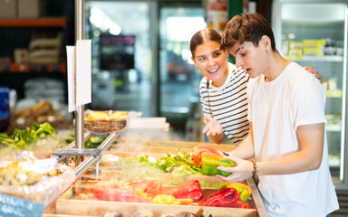Young woman and young man shoppers choosing bell peppers in grocery store..