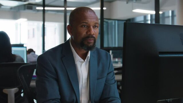 Mature black man in businesswear typing on computer at desk in office