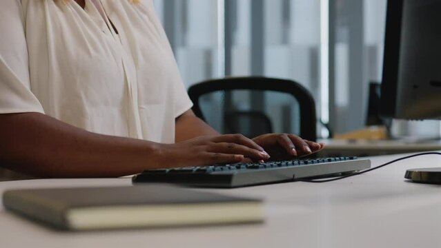 Close-up of mid adult black woman in blouse using computer at desk in office
