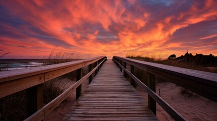 The wooden bridge extends onto the sandy beach, under a sky painted with shades of orange and pink