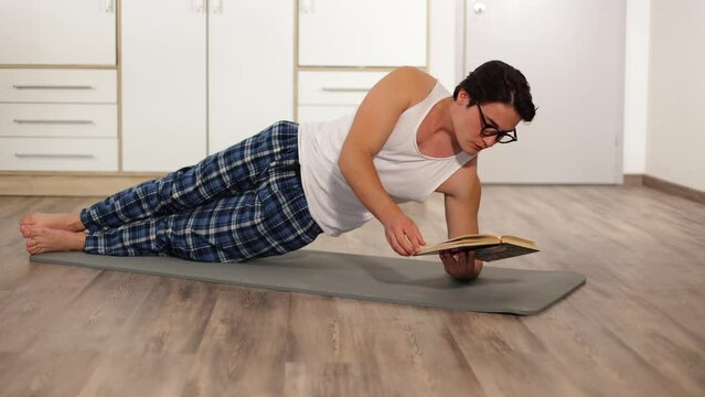athletic man is doing exercises standing in side elbow plank at home read book