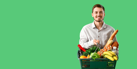 Man holding shopping basket full of products on green background with space for text
