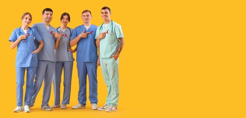 Group of doctors with red ribbons on yellow background with space for text. World AIDS Day