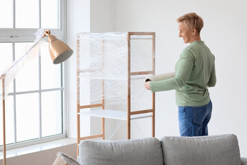 Mature woman wrapping shelving unit with stretch film at home
