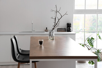 Vase with tree branches and glass of coffee on island in modern kitchen