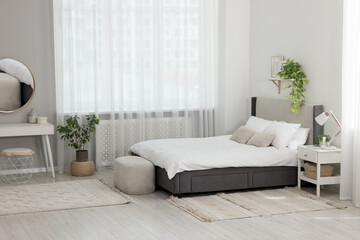 Stylish bedroom interior with large comfortable bed and ottoman near window