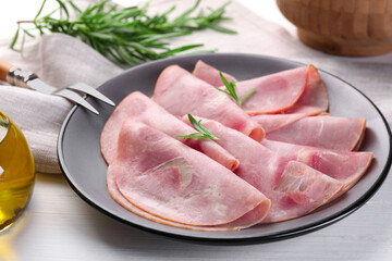 Tasty ham with rosemary and carving fork on white wooden table, closeup