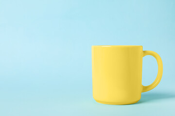 One yellow ceramic mug on light blue background, space for text