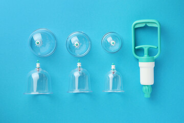 Plastic cups and hand pump on light blue background, flat lay. Cupping therapy